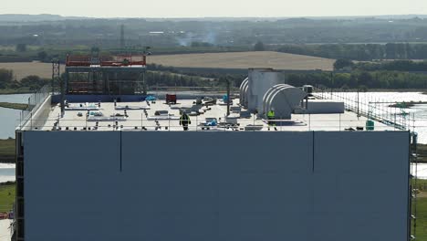 Static-aerial-view-of-two-construction-workers-on-a-power-station-rooftop-in-protective-clothing