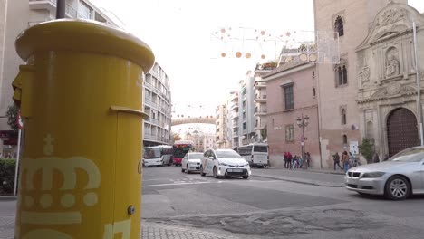 Car-drives-through-intersection-past-yellow-letterbox-in-downtown-Seville,-Spain