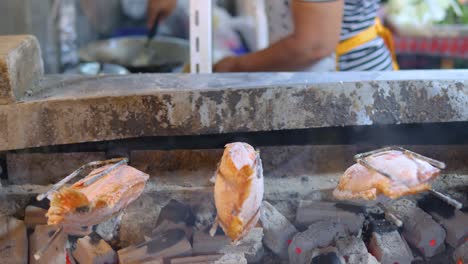 Pescado-De-Pargo-Rojo-Cocinando-Y-Girando-Sobre-Carbón-Caliente,-Fondo-De-Cocina-De-Trabajadores,-Mercado-Nocturno