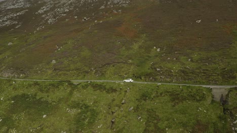 single-white-car-making-its-way-through-rural-Irish-roads,-aerial