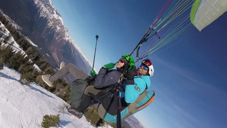 Aerial-view-side-shot,-tandem-Paragliding-above-the-snowy-mountains-in-Trentino,-Italy,-skier-skiing-down-the-slopes