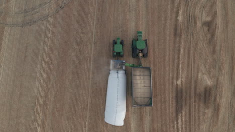 Drone-view-of-full-grain-cart-tractor-dumping-grain-in-temporary-silo-bag