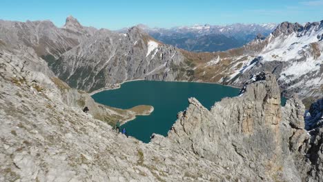 Aerial-shot-of-a-group-of-friends-sitting-together-on-top-of-the-mountain-Lunersee,-looking-over-Love-Heart-lake-after-a-long-hike-through-the-Swiss-alps-during-a-summer-hiking-trip