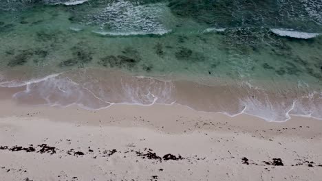 Aerial-drone-looking-straight-down-over-crystal-clear-waves-crashing-into-an-empty-paradise-beach-in-Cozumel-island-in-Mexico