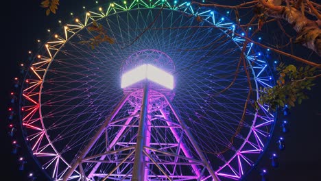 Wide-Exterior-Night-Time-Shot-of-a-Big-Wheel-Slowly-Spinning-as-Its-Colours-Change-on-its-Metal-Exterior