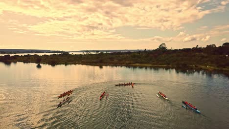 Aerial-view-group-of-rowing-sport-team-athletes-performing-lap-around-lake-buoy-in-long-boats-at-sunrise