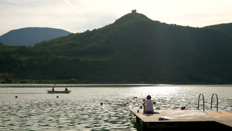 Frau-Sitzt-Auf-Einem-Holzsteg-Und-Entspannt-Sich-Und-Genießt-Den-Sonnenaufgang-Mit-Der-Kanu-Silhouette-Im-Hintergrund