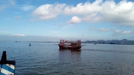 Port-of-Hai-Phong-Vietnam-with-red-fishing-ship-passing-by-on-cloudy-day,-Handheld-shot