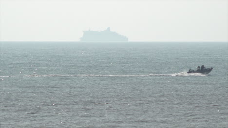 A-UK-Border-Force-rib-speed-boat-patrols-The-Channel-just-off-the-coastline-of-Kent-in-front-of-a-Dover-to-Calais-transport-and-passenger-ferry-heading-towards-France
