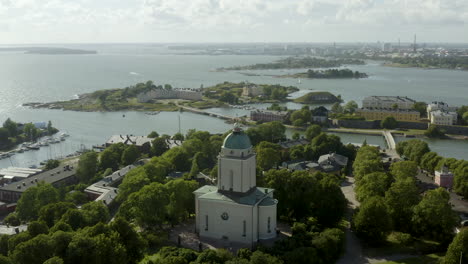 Aerial-view-around-the-church,-at-the-Suomenlinna-island-the-Helsinki-cityscape-in-the-background,-sunny,-summer-day,-in-Helsingfors,-Finland---orbit,-drone-shot