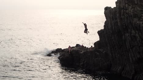 Young-man-jumping-into-water-of-coast-of-Riomaggiore-at-sunset