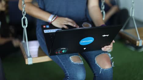 Worker-at-a-trendy-startup-office-works-on-her-computer-while-sitting-on-a-swing