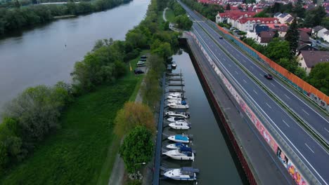 Aerial-view-overlooking-boats-parked-on-the-side-of-the-Main-river-and-traffic-on-road-43,-in-Raunheim-town,-Germany---tilt-up,-drone-shot