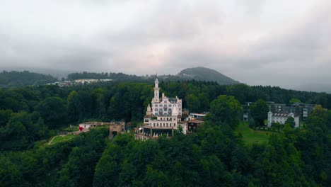 Drone-shot-over-forest-towards-the-white-Chateau-Gutsch-castle-and-luxury-hotel,-dark,-gloomy,-overcast-day,-in-Luzern,-Switzerland---rising,-aerial-view