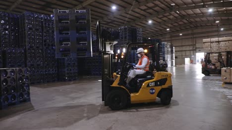 Forklift-truck-driver-loading-gallon-water-bottle-stack-onto-industrial-warehouse-conveyor-belt-slow-motion