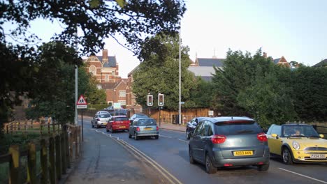 SLOWMO-4k-street-with-medium-traffic,-trees-in-the-foreground,-day,-Cambridge,-England