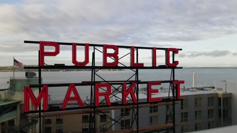 Public-Market-sign-atop-the-iconic-Pike-Place-Market,-Puget-Sound-as-background,-aerial