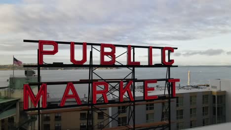 Cartel-Del-Mercado-Público-En-La-Cima-Del-Icónico-Mercado-Pike-Place,-Puget-Sound-Como-Fondo,-Antena