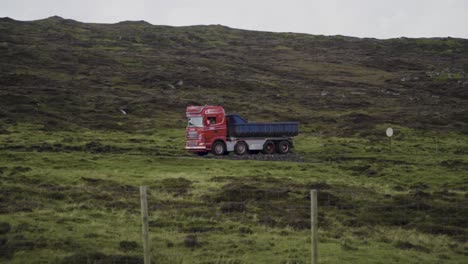 Slow-motion-tracking-shot-of-truck-driving-between-green-hills-on-Faroe-Islands-during-clouds-at-sky
