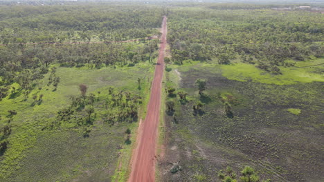 High-Slow-Moving-Drone-shot-of-Empty-Straight-Red-Road-and-Green-Bushland-Near-Holmes-Jungle-Nature-Park,-Darwin,-Northern-Territory