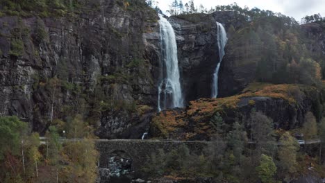 Aufsteigende-Luftaufnahme-Des-Wasserfalls-Hesjedalsfossen-Und-Der-Alten-Steinbrücke---Norwegen