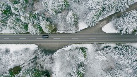 Direkt-Von-Oben-–-Ein-Schnell-Fahrendes-Auto-Rast-Durch-Eine-Winterliche-Waldlandschaft-Mit-Aufnahmen-Von-Schneebedeckten-Bäumen-Neben-Einer-Straße-Von-Oben-Nach-Unten