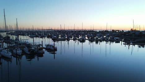 A-rising-high-view-of-an-early-morning-sunrise-over-a-calm-boat-harbor-full-of-recreational-boats-and-vehicles
