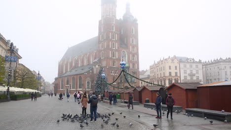 Tourists-feeding-pigeons-on-Main-Market-Square,-Krakow-next-to-Saint-Mary-Church