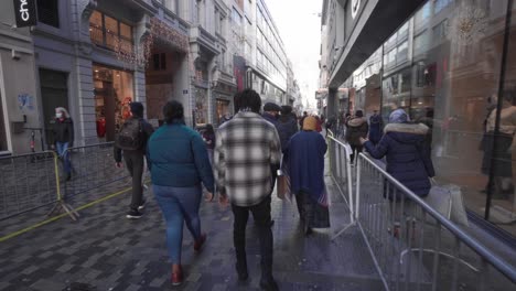 Crowds-of-visitors-walk-through-popular-shopping-street-Rue-Neuve-in-Brussels,-they-are-wearing-compulsory-face-masks-due-to-local-Covid-19-regulation
