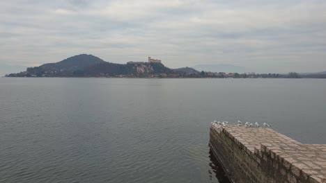 Flock-of-seagulls-on-pier-boardwalk-on-Maggiore-lake-with-Angera-fortress-in-background