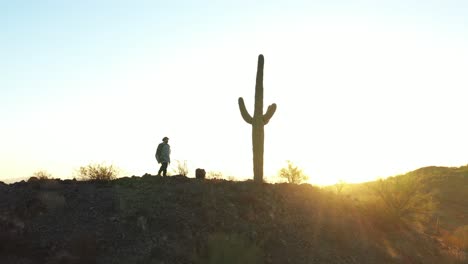 A-wild-west-desperado-wearing-a-poncho-walks-along-a-desert-ridgeline-past-a-Saguaro-cactus