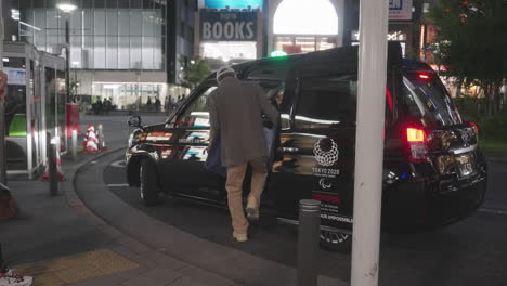 Couple-Wearing-Mask-Getting-On-A-Taxi-With-Tokyo-2020-Logo-On-It-At-Night-During-Pandemic