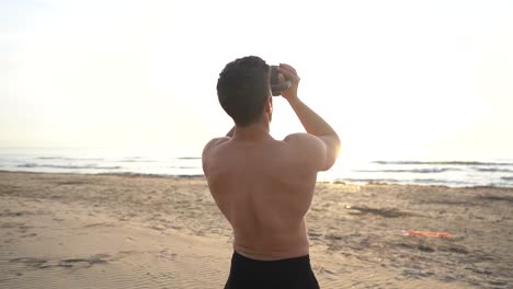 Shirtless-man-training-with-kettlebell-on-the-beach-at-sunrise-in-slow-motion
