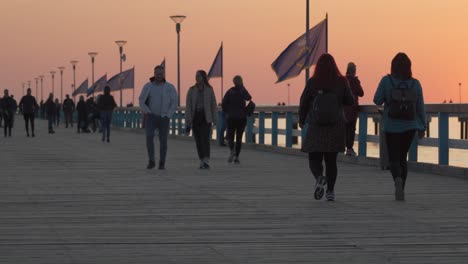 People-Walking-on-Palanga-Pier-on-Golden-Hour-Evening-with-Sun-Setting-in-Sky-and-Flags-Waving-in-Wind