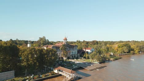 Aerial-orbit-of-Tigre-exclusive-rowing-club-beside-de-la-Plata-river-surrounded-by-trees-at-golden-hour,-Buenos-Aires