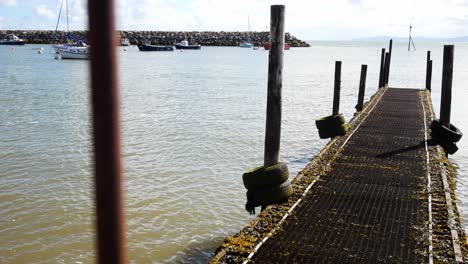 Entspannender-Holzsteg-Am-Hafen,-Gehweg,-Ruhige-Szene-über-Blauem-Himmel,-Ruhiges-Meer,-Gezeiten,-Rechts-Dolly,-Vorbei-An-Zaunstangen