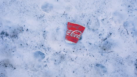 Rotating-overhead-shot-of-flat-red-paper-Coca-Cola-mug-on-snowy-ground