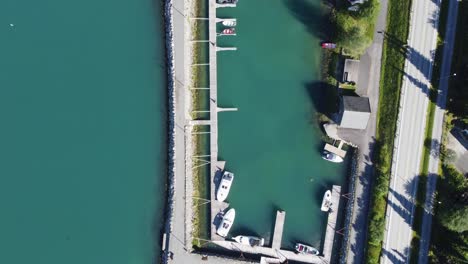 Idyllic-pleasure-craft-marina-in-Loen-Norway---Beautiful-top-down-aerial-showing-turquoise-colored-water-and-marina-in-between-breakwater-and-countryside-road---Summer-with-seagulls-flying-around