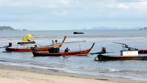 Vista-De-Los-Barcos-De-Pesca-Amarrados-A-Lo-Largo-De-Una-Playa-Azotada-Por-El-Viento-Durante-El-Día-En-El-Sur-De-Satun,-Tailandia