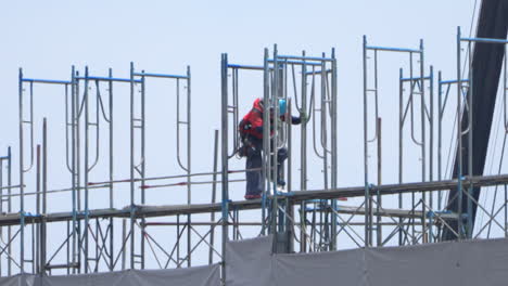 Manual-Worker-In-Hard-Hat-Working-Alone-On-Scaffoldings-At-The-Construction-Site