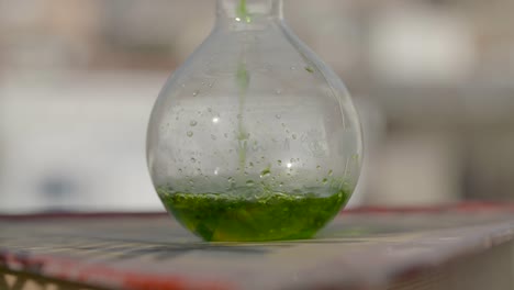 Bunte-Grüne-Flüssige-Lösung-In-Zeitlupe,-Die-In-Eine-Kugelförmige-Glasbehälterflasche-Gegossen-Wird