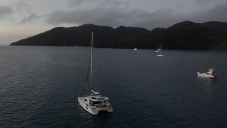 Morning-dawn-aerial-orbits-rental-catamaran-sailboat-moored-off-shore