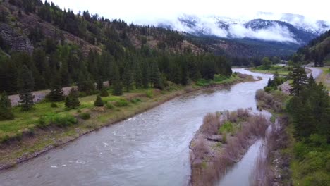 Disparo-De-Un-Dron-En-Movimiento-Lento-Del-Río-Con-Montañas-Recién-Cubiertas-De-Nieve-En-El-Fondo