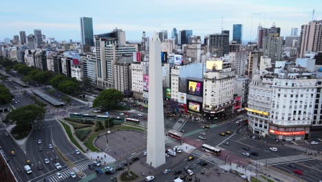 Aerial-slow-pull-out-shot-of-busy-intersection-traffics-with-dense-commercial-and-residential-buildings-and-billboards-at-Republic-Square-with-iconic-monumental-Obelisco-structure-in-the-center