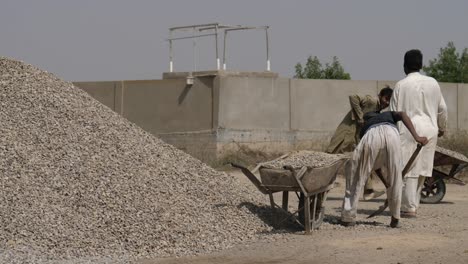 Manual-Labourer-Using-Shovel-To-Fill-Aggregate-In-Wheelbarrow-In-Karachi,-Pakistan