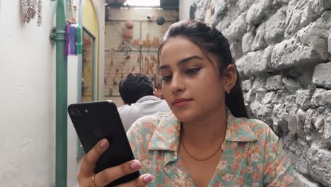 Una-Hermosa-Joven-Con-El-Pelo-Largo-Y-Negro-Sentada-En-Una-Cafetería-Y-Usando-Un-Teléfono-Inteligente-O-Un-Teléfono-Celular