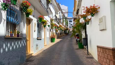 Walking-in-a-typical-Spanish-street-in-old-city-Estepona-with-houses,-colorful-flower-pots-and-beautiful-balconies