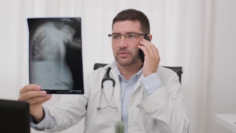 Arzt-Spricht-Auf-Dem-Smartphone,-Während-Er-Sich-Einen-Röntgenfilm-Ansieht