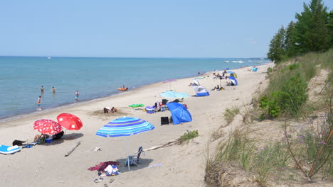 Turistas-Y-Coloridas-Sombrillas-En-La-Orilla-Arenosa-En-El-Lago-Huron,-Ontario,-Canadá