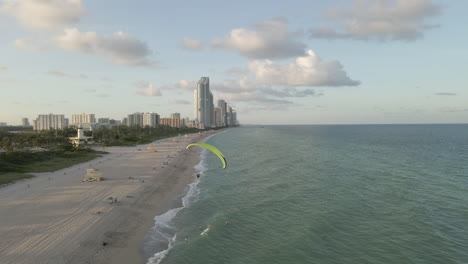 Aerial-follows-acrobatic-paramotor-flight-over-Haulover-Beach,-Miami